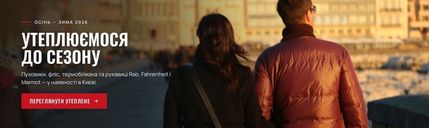Пара в утеплених куртках гуляє набережною міста на заході сонця